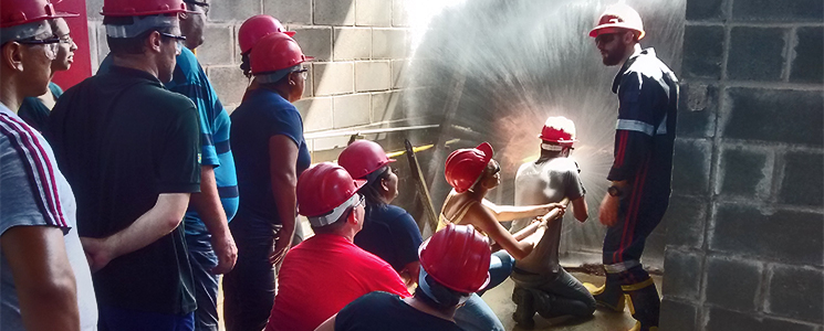 Alunos vestidos de vermelho e capacetes jogando água em ponto de incêndio Alunos vestidos de vermelho e capacetes jogando água em ponto de incêndio