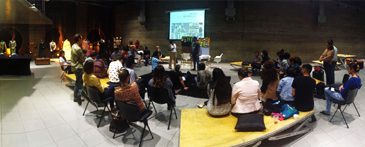 Panorama de roda de conversa mostrando audiência em ao redor de palestrante em frente à telão Panorama de roda de conversa mostrando audiência em ao redor de palestrante em frente à telão