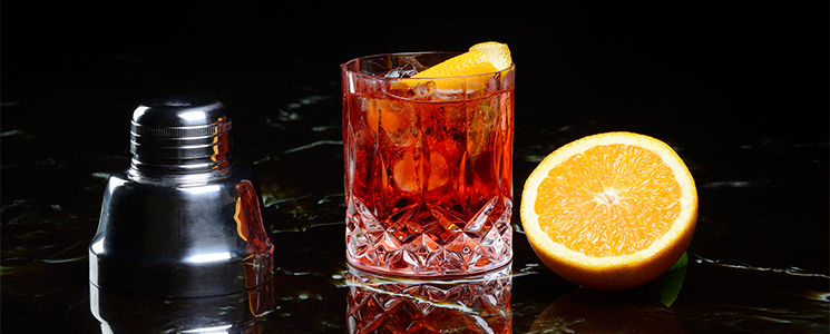 Tampa metálica de coqueteleira, copo de vidro com drink e metade de laranja sobre fundo preto. Tampa metálica de coqueteleira, copo de vidro com drink e metade de laranja sobre fundo preto.