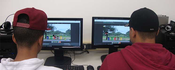 Dois alunos lado a lado jogando os jogos com monitores de computador à frente Dois alunos lado a lado jogando os jogos com monitores de computador à frente