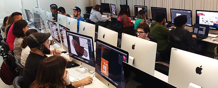 Divididos em duas mesas, alunos mexem em computadores lado a lado Divididos em duas mesas, alunos mexem em computadores lado a lado
