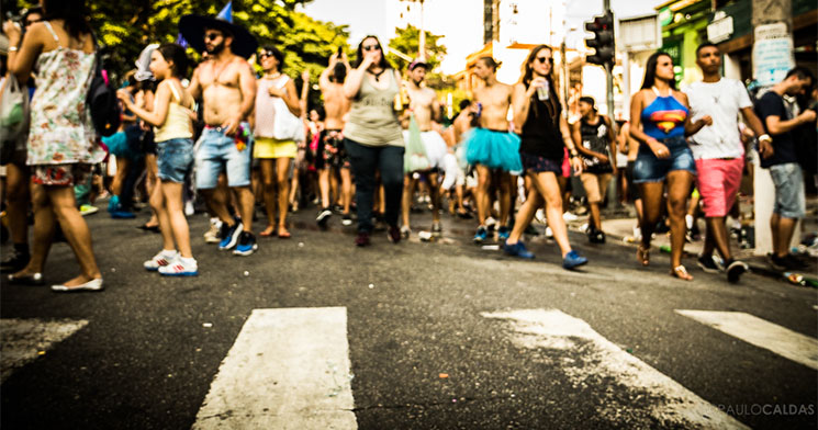 Asfalto com faixa de pedestre em primeiro plano e foliões desfocados em plano de fundo Asfalto com faixa de pedestre em primeiro plano e foliões desfocados em plano de fundo