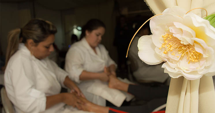 Detalhe da decoração do Spa Day Urbano organizado pelo curso Técnico em Estética do Senac Santana com flores naturais e tecidos à direita, alunas de jaleco executando atendimento em cliente, ao fundo, desfocadas Detalhe da decoração do Spa Day Urbano organizado pelo curso Técnico em Estética do Senac Santana com flores naturais e tecidos à direita, alunas de jaleco executando atendimento em cliente, ao fundo, desfocadas