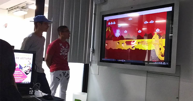 Dois alunos dos cursos Técnico em Multimídia e em Programação de Jogos Digitais do Senac Largo Treze, em frente à televisão em sala de aula, apresentando jogos digitais desenvolvidos por meio de parceria entre as turmas Dois alunos dos cursos Técnico em Multimídia e em Programação de Jogos Digitais do Senac Largo Treze, em frente à televisão em sala de aula, apresentando jogos digitais desenvolvidos por meio de parceria entre as turmas