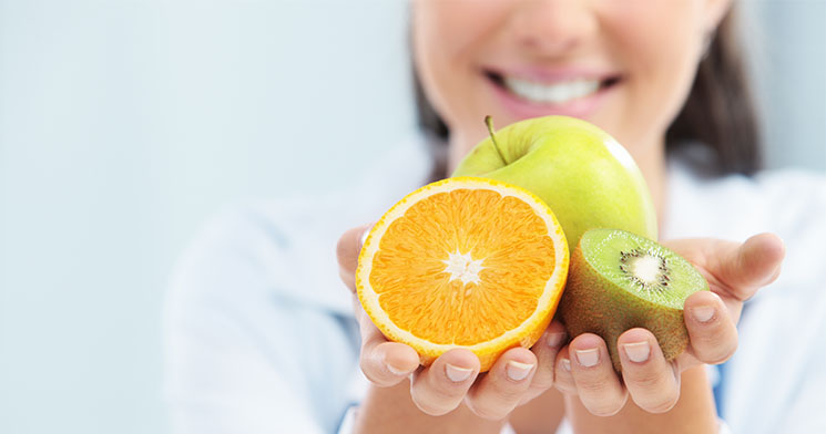 Mulher sorri e segura maçã, laranja e kiwi Mulher sorri e segura maçã, laranja e kiwi