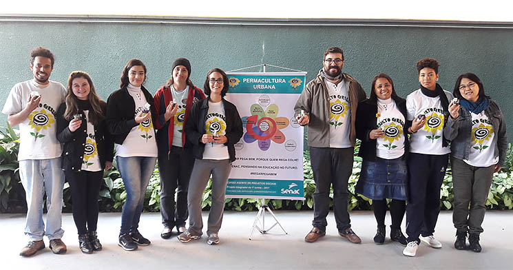 Alunos do curso Agente de Projetos Ambientais em frente à mural e cartazes que apresentam o Projeto Girassol de aplicação da permacultura em espaços urbanos comunitários Alunos do curso Agente de Projetos Ambientais em frente à mural e cartazes que apresentam o Projeto Girassol de aplicação da permacultura em espaços urbanos comunitários
