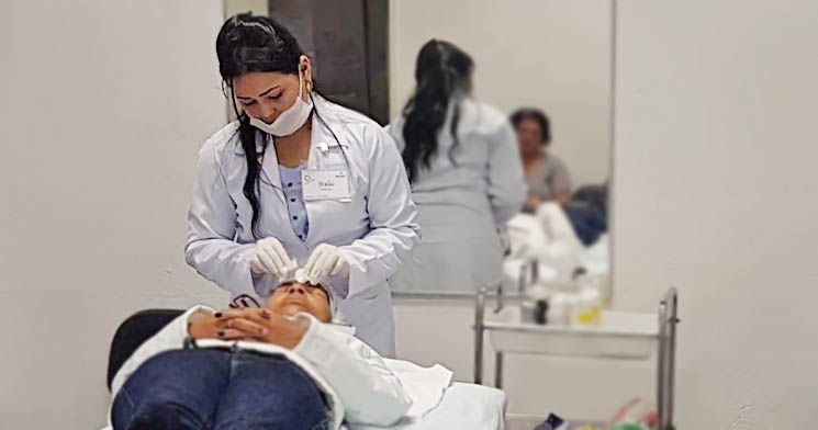 Aluna de jaleco branco realiza procedimento estético facial em mulher deitada sobre uma maca Aluna de jaleco branco realiza procedimento estético facial em mulher deitada sobre uma maca