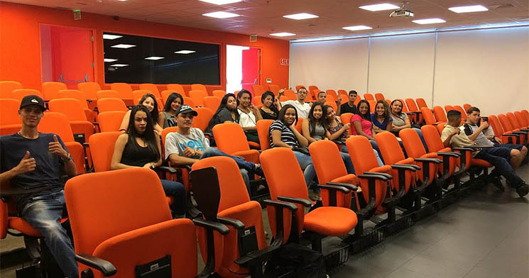 Alunos sentados em poltronas alaranjadas do auditório da empresa visitada Alunos sentados em poltronas alaranjadas do auditório da empresa visitada