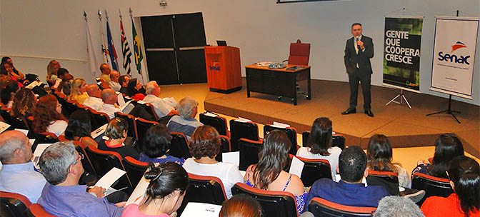 Palestrante no palco do auditório do Senac Guaratinguetá fala ao público do evento Palestrante no palco do auditório do Senac Guaratinguetá fala ao público do evento
