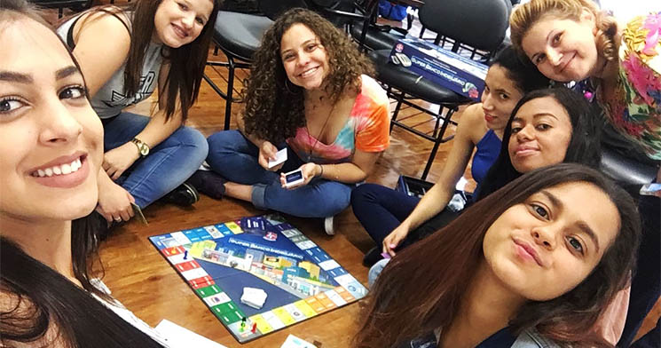 Jovens do programa Aprendizagem sentados ao redor de tabuleiro do Banco Imobiliário Jovens do programa Aprendizagem sentados ao redor de tabuleiro do Banco Imobiliário