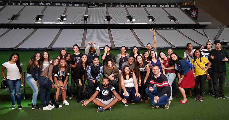 Alunos das turmas do curso Técnico em Administração do Senac Itaquera enfileirados e sorridentes no campo da Arena Corinthians, com arquibancadas do estádio ao fundo Alunos das turmas do curso Técnico em Administração do Senac Itaquera enfileirados e sorridentes no campo da Arena Corinthians, com arquibancadas do estádio ao fundo