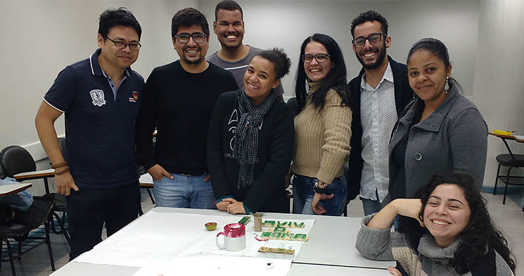 Alunos do Senac Largo Treze sorriem lado a lado ao redor de mesa com matrizes de impressão caseiras Alunos do Senac Largo Treze sorriem lado a lado ao redor de mesa com matrizes de impressão caseiras