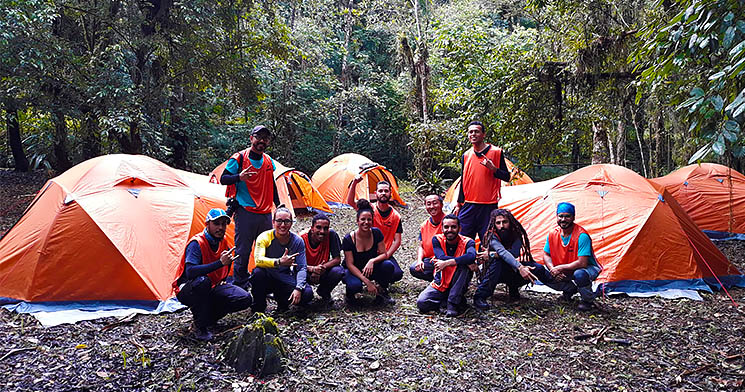 Alunos ajoelhados em frente às barracas de camping montadas em meio à floresta Alunos ajoelhados em frente às barracas de camping montadas em meio à floresta