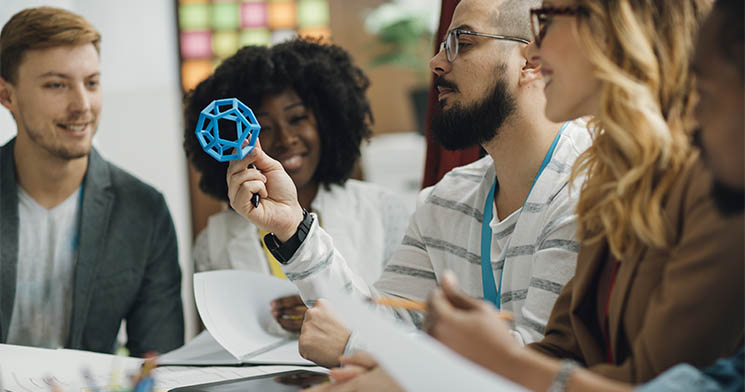 Jovem segura forma geom?trica vazada na cor azul e ? observado por colegas em sala de aula Jovem segura forma geom?trica vazada na cor azul e ? observado por colegas em sala de aula