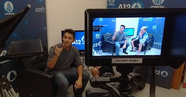 Tela de câmera filmadora mostra dois alunos simulando um programa de entrevista em estúdio de TV da agência A12 Tela de câmera filmadora mostra dois alunos simulando um programa de entrevista em estúdio de TV da agência A12