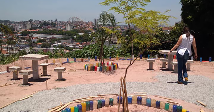 Mulher anda em terreno com mudas de árvores, mesa e banco Mulher anda em terreno com mudas de árvores, mesa e banco