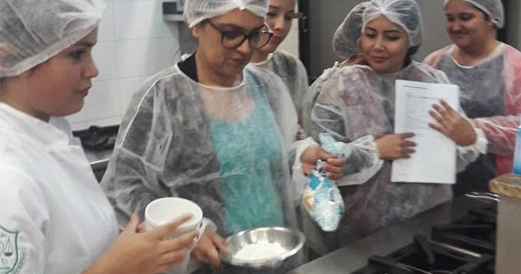 Estudantes paramentados com equipamentos de higiene preparando pão na cozinha Estudantes paramentados com equipamentos de higiene preparando pão na cozinha