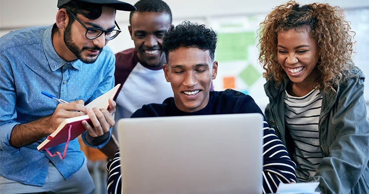Imagem de quatro jovens sorridentes observando tela de um computador Imagem de quatro jovens sorridentes observando tela de um computador