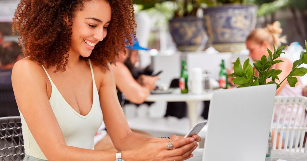 Foto de jovem negra no computador e celular em mesa de lanchonete. Foto de jovem negra no computador e celular em mesa de lanchonete.