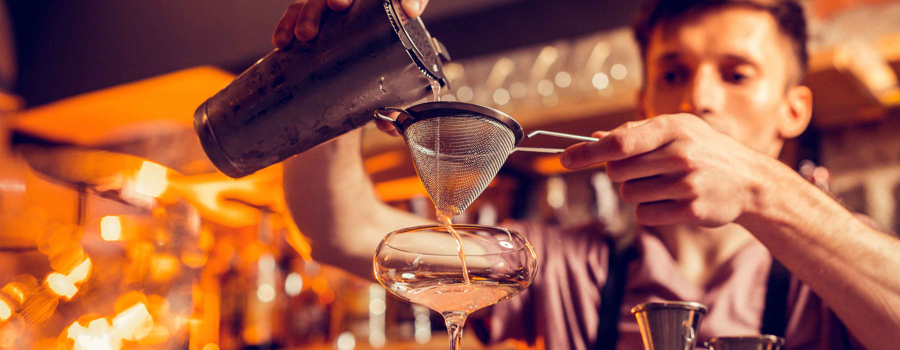 Formação de Bartender: preparo e serviço de coquetéis - Foto de um homem preparando um coquetel em uma taça