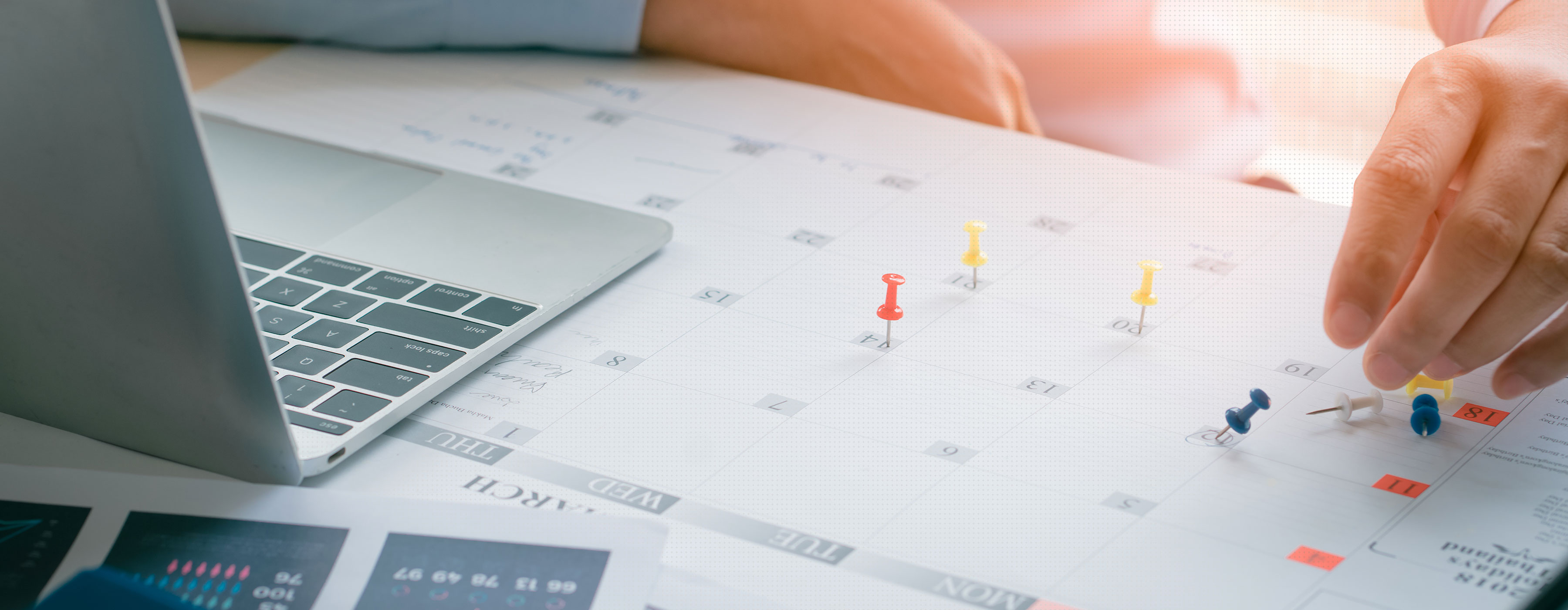 Foto em close das mãos de uma pessoa sinalizando compromissos em calendário em cima da mesa.