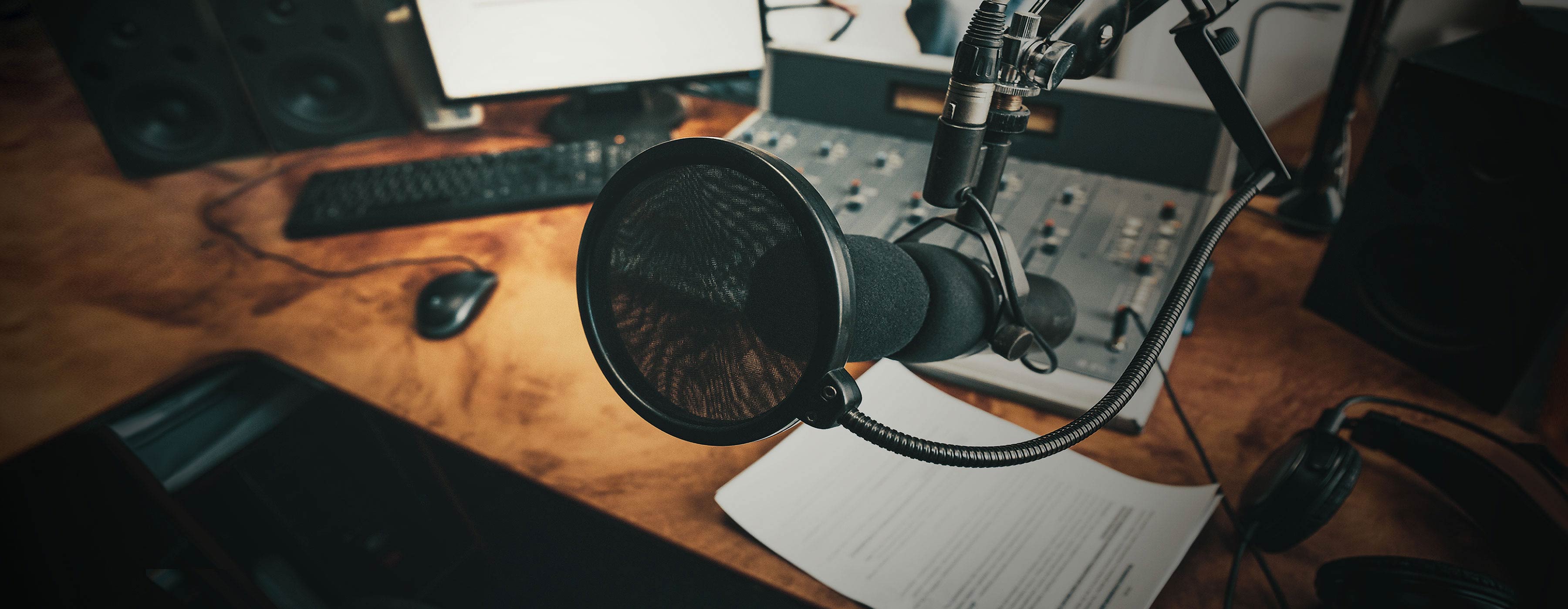 Prática de Locução de Rádio - Foto de uma mesa de trabalho com um microfone e equipamentos para locução