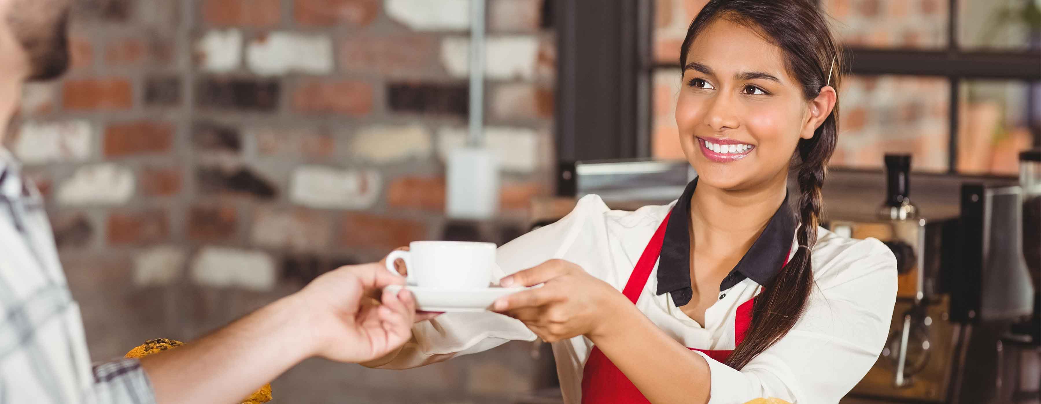 Atendente de Lanchonete - Foto de uma mulher sorrindo e servindo café para um cliente