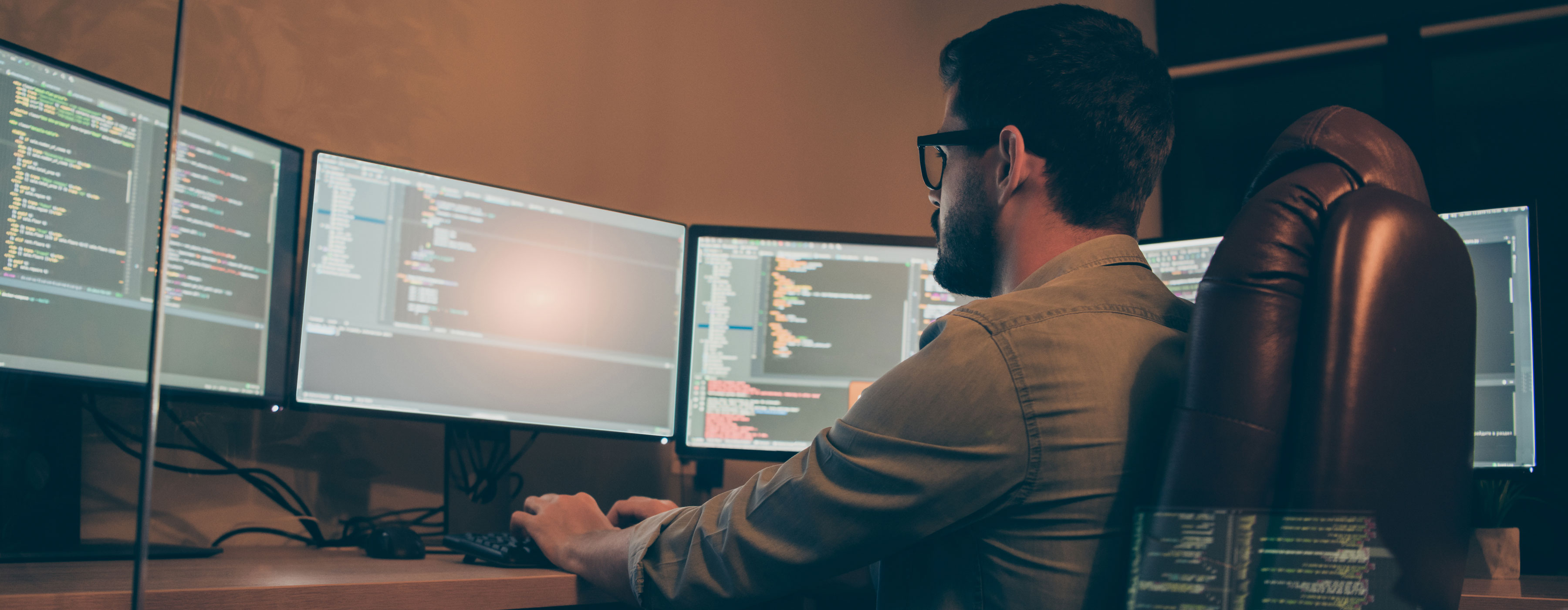 Administração do MYSQL - foto de um homem sentado, olhando para algumas telas de computadores  digitando.