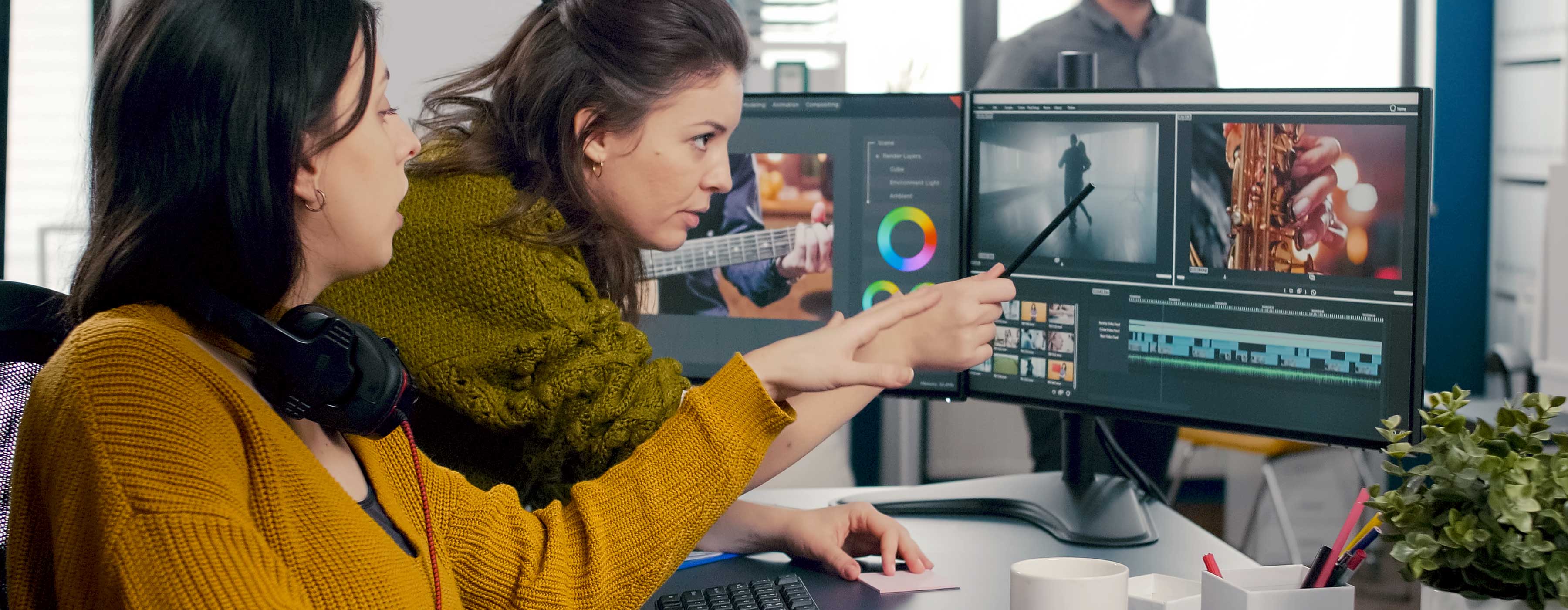 Foto de duas mulheres olhando para imagens em software de edição de vídeo em duas telas de computador.
