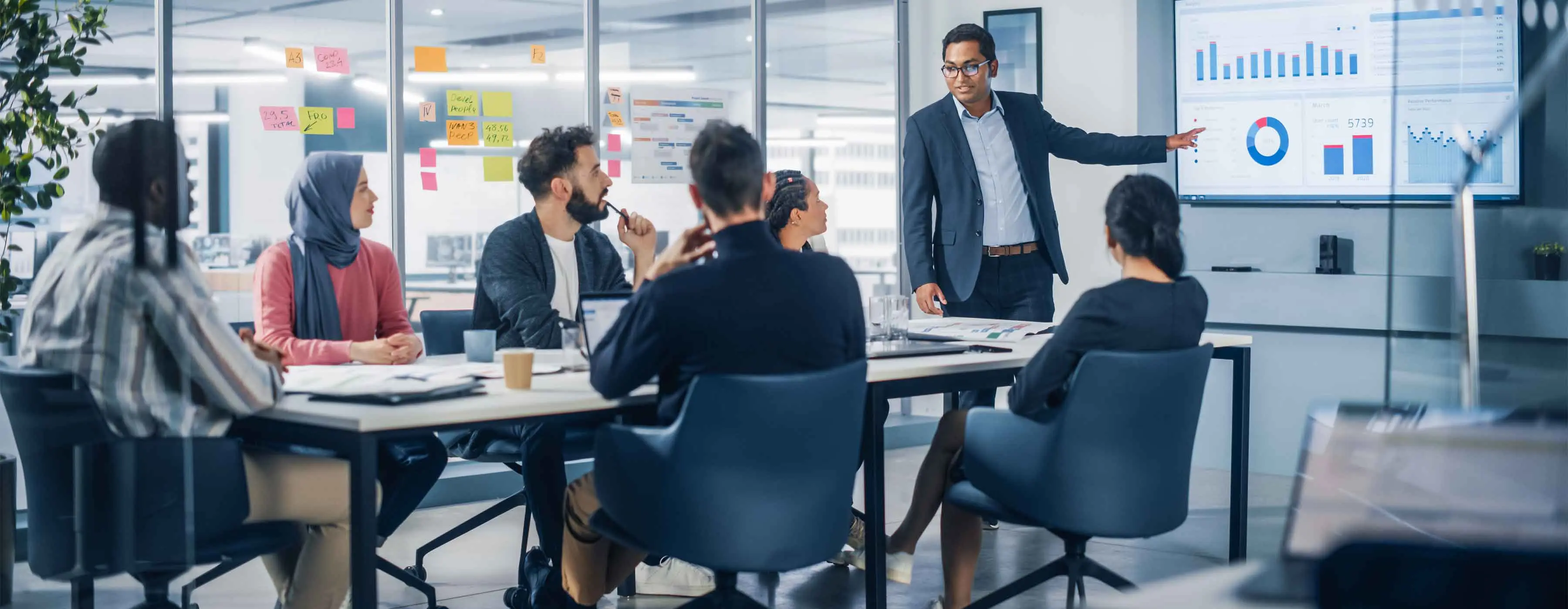 Além do Ganha-Ganha - Negociações em Situações Desafiadoras - Grupo diverso de pessoas acompanhando um homem apresentando gráficos em um painel.