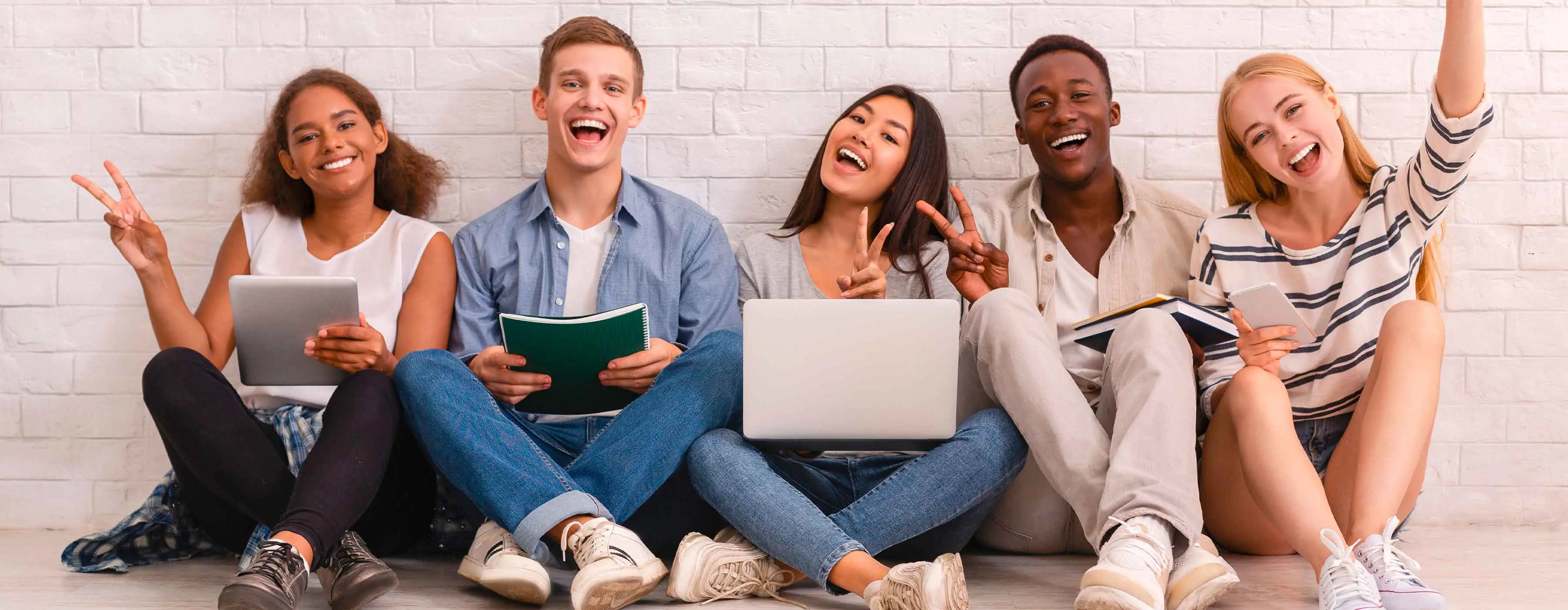 Francês Intermediário - níveis 1, 2 e 3. Foto de 5 jovens sentados no chão, sorrindo, segurando cadernos, livros, tablet e notebook.