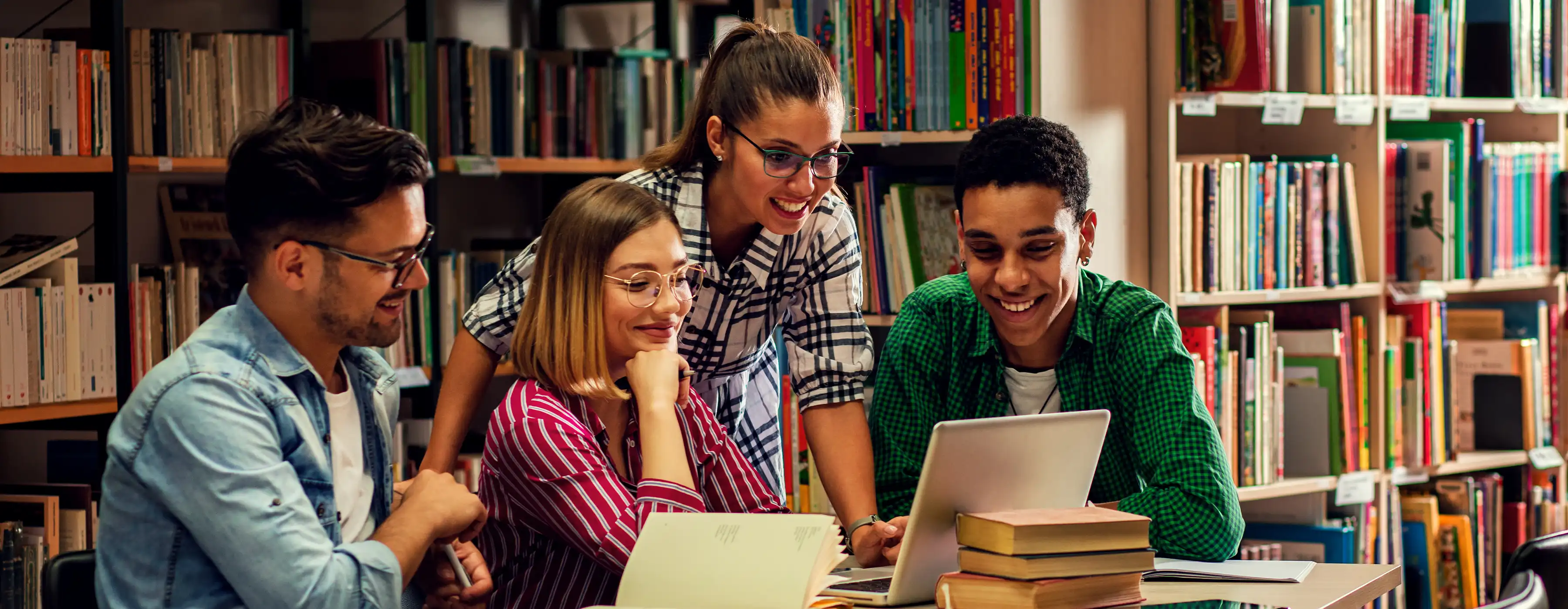 foto de quatro pessoas em uma biblioteca olhando um notebook