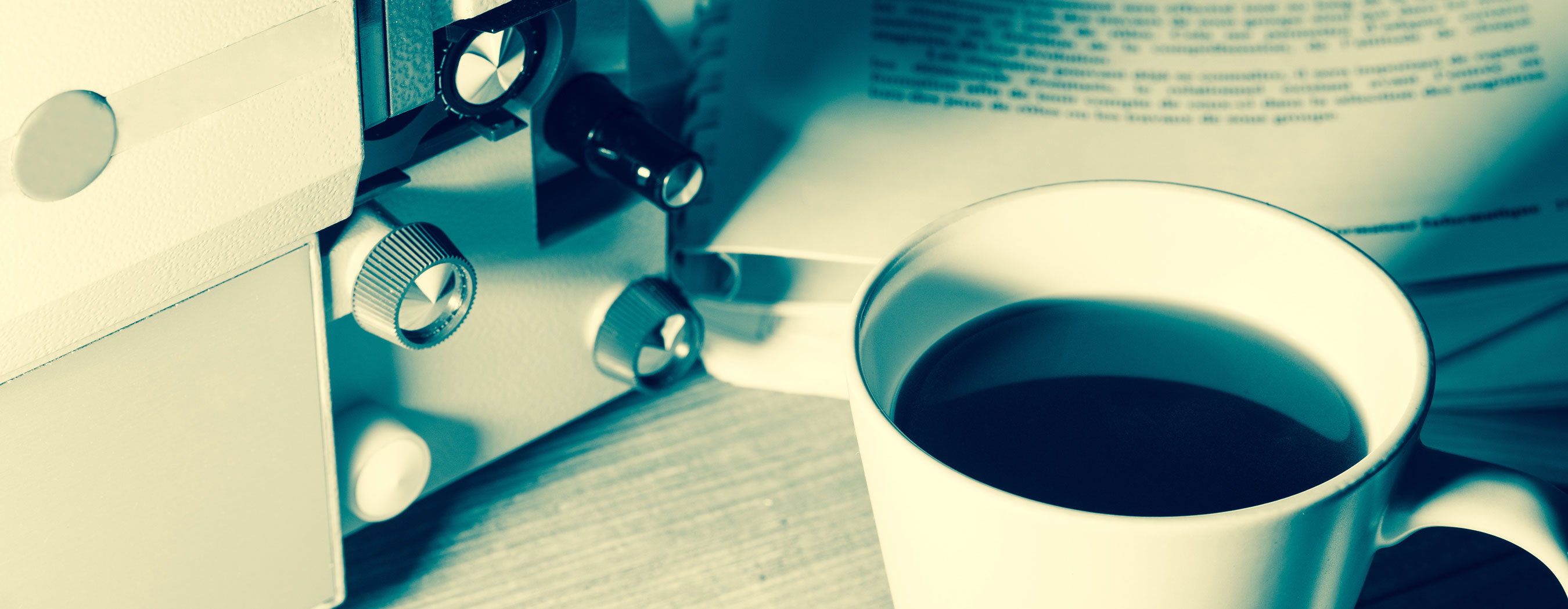 Foto em close de uma xícará de café próxima a uma câmera de filmagem e um caderno com roteiros escritos.