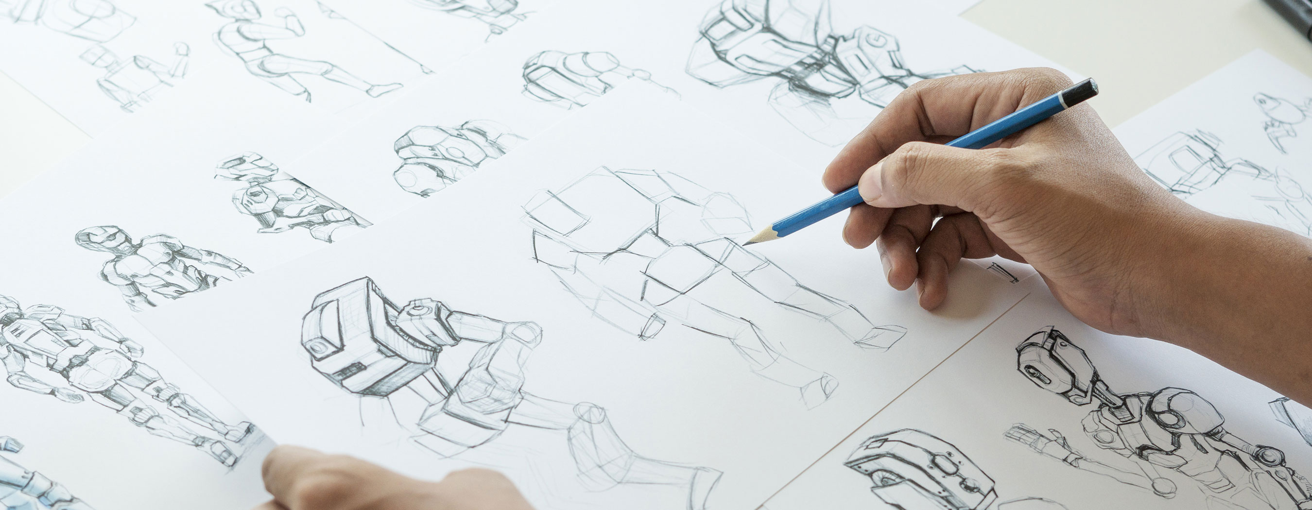 Foto em close das mãos de uma pessoa desenhando a lápis vários modelos de robôs.