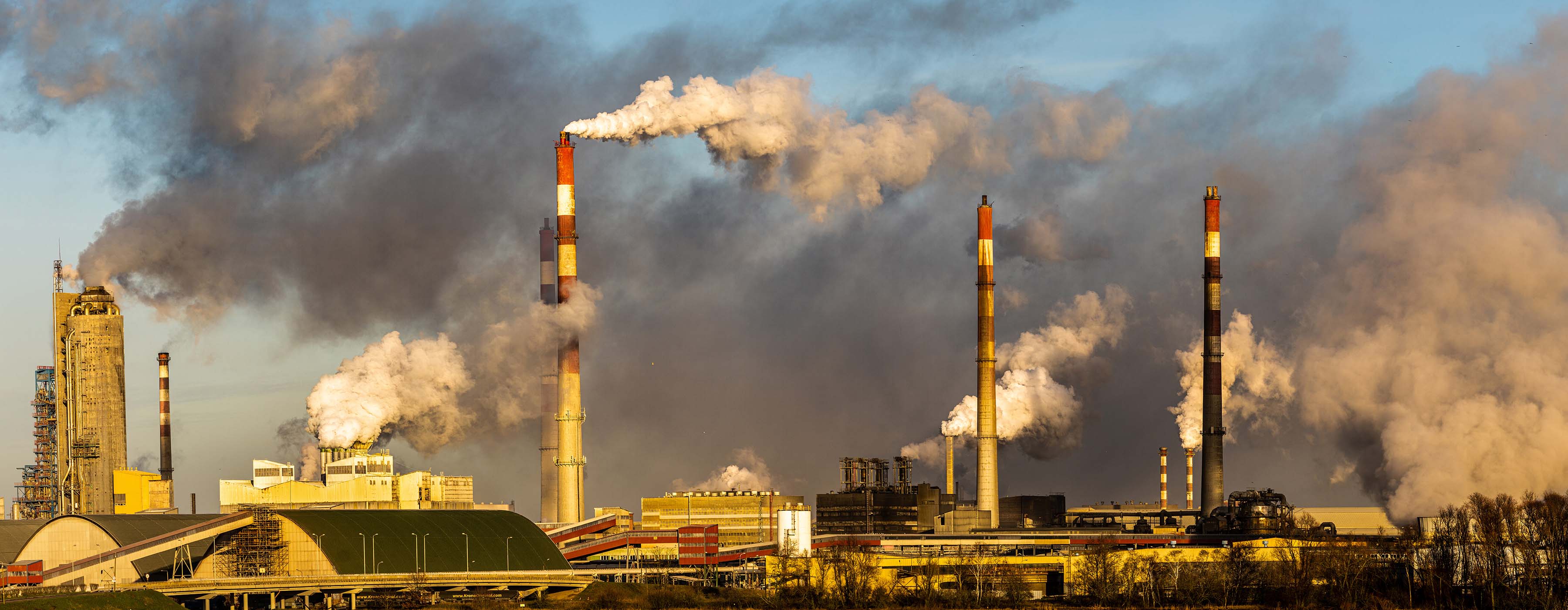 Foto de várias chaminés industriais jogando muita fumaça no ar.