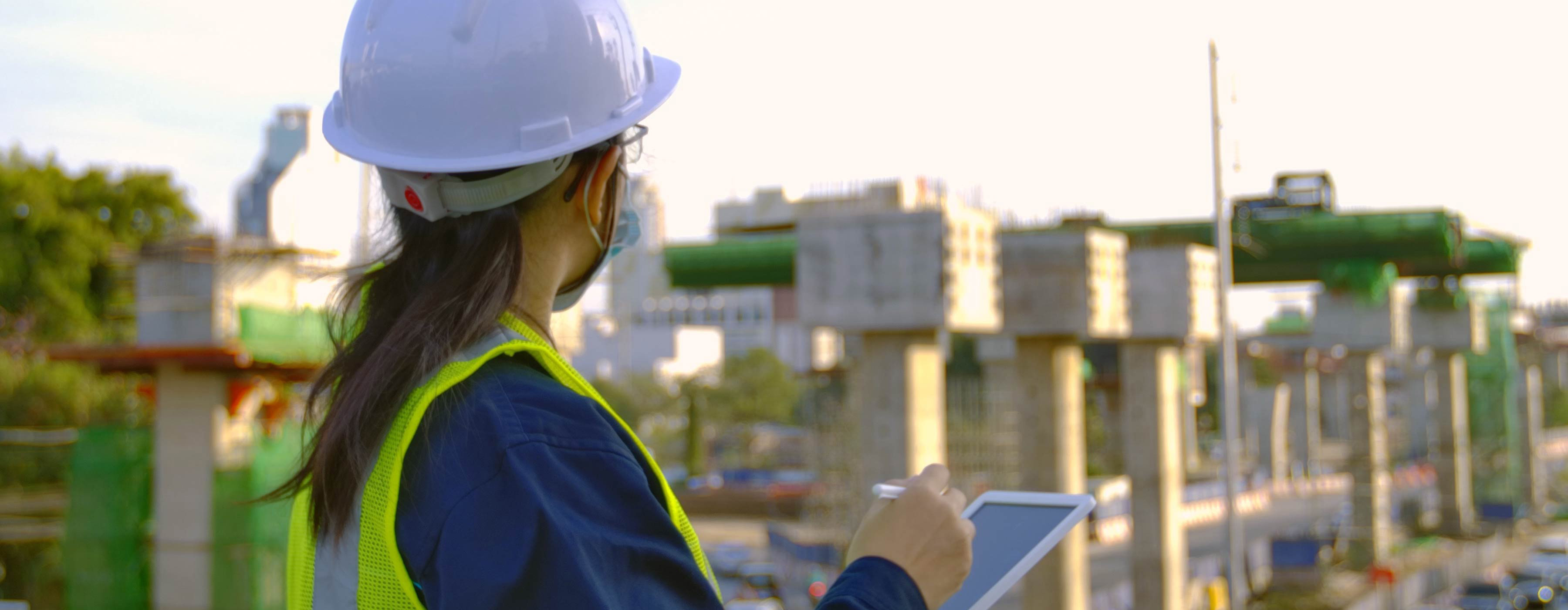 Formação de Auditor Ambiental - foto de mulher uniformizada, com máscara e capacete de proteção, de lado olhando horizonte em obra de construção.