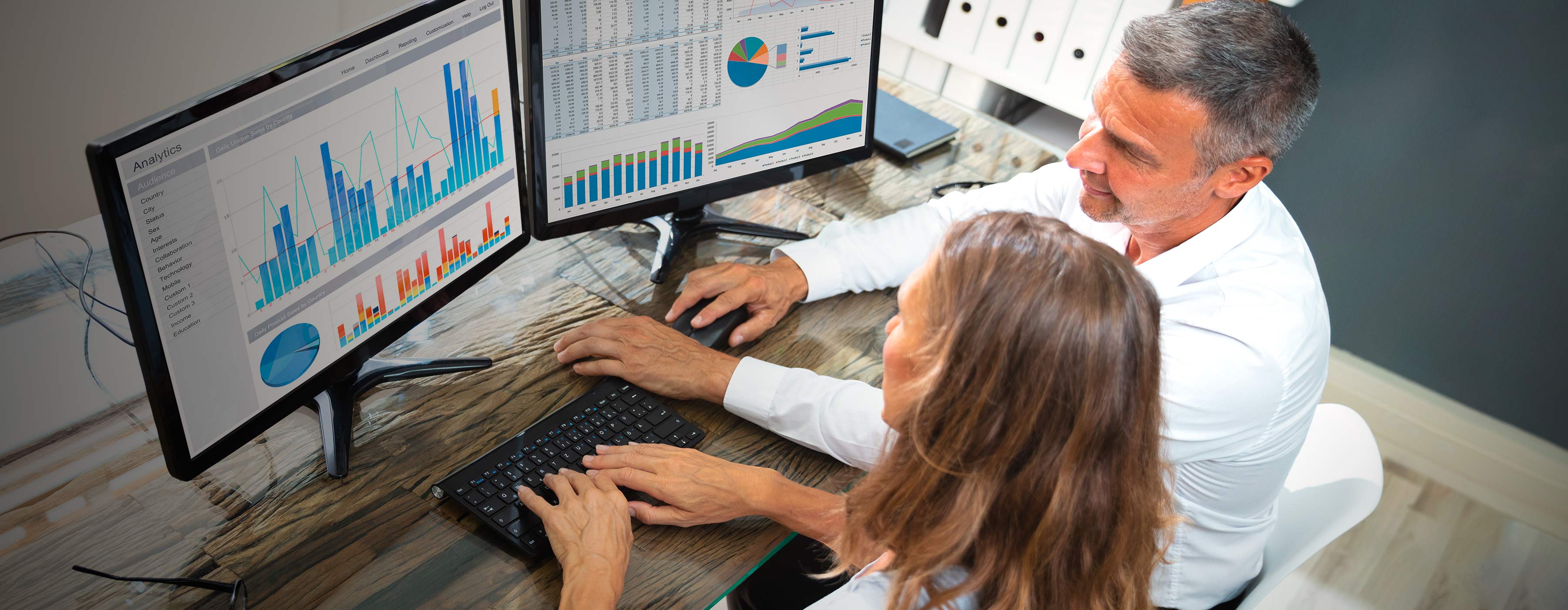 Ferramentas e Métricas (Data Driven) - foto de duas pessoas editando um gráfico na frente de duas telas de computador em um escritório.