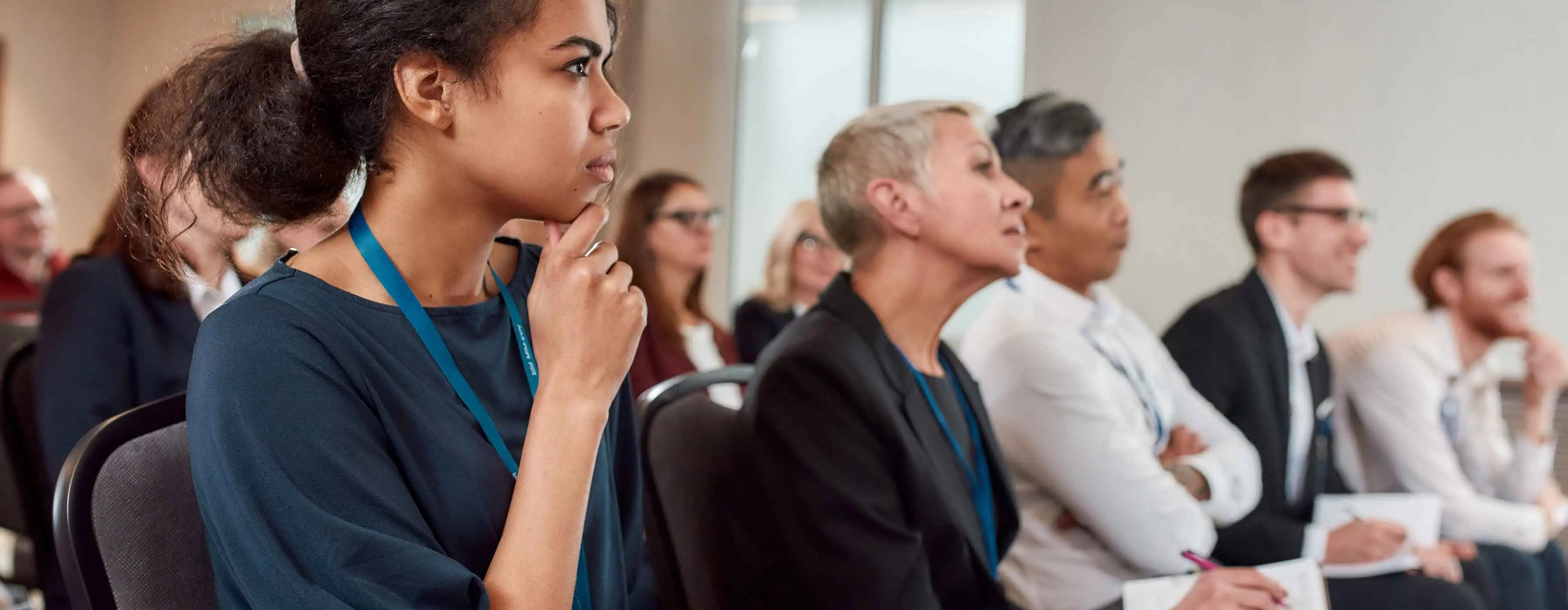 Eventos, Marketing Cultural e Patrocínios - foto de grupo de pessoas sentadas olhando para a mesma direção, e em primeiro plano, uma mulher que toca o próprio queixo