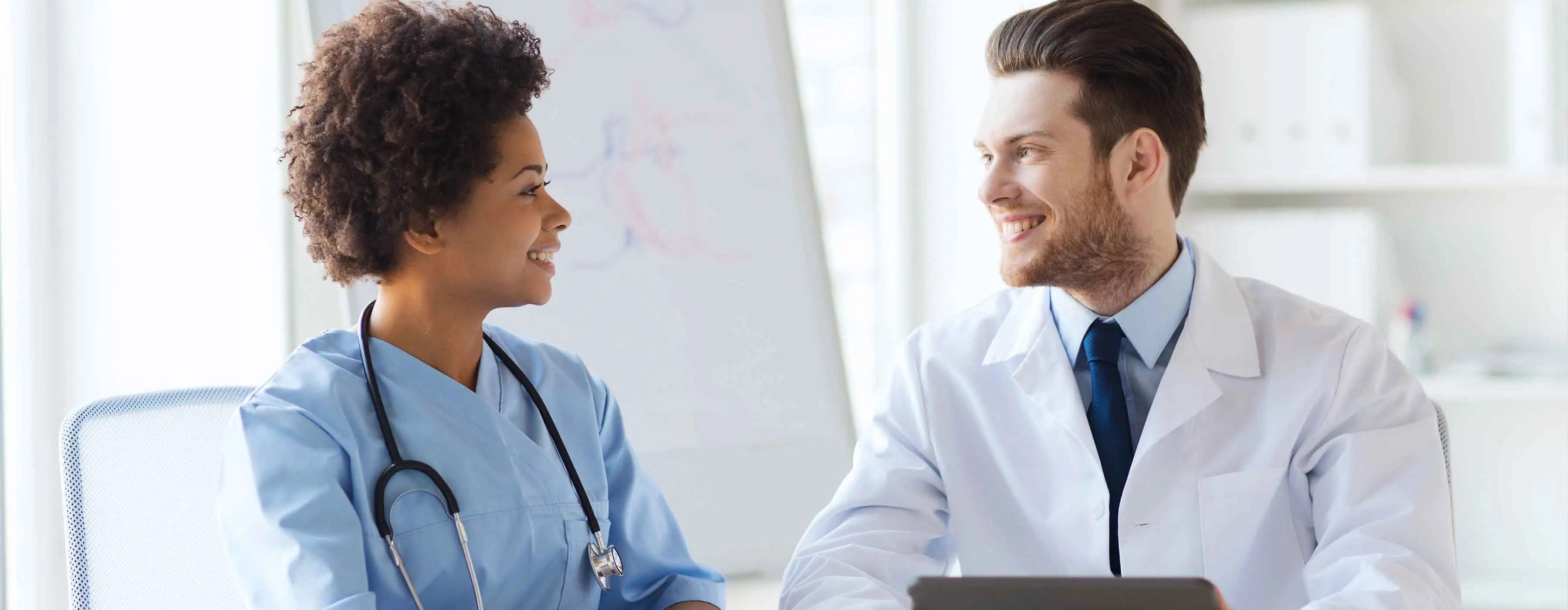 Foto de dois profissionais da saúde, uma mulher e um homem, conversando em ambiente hospitalar 