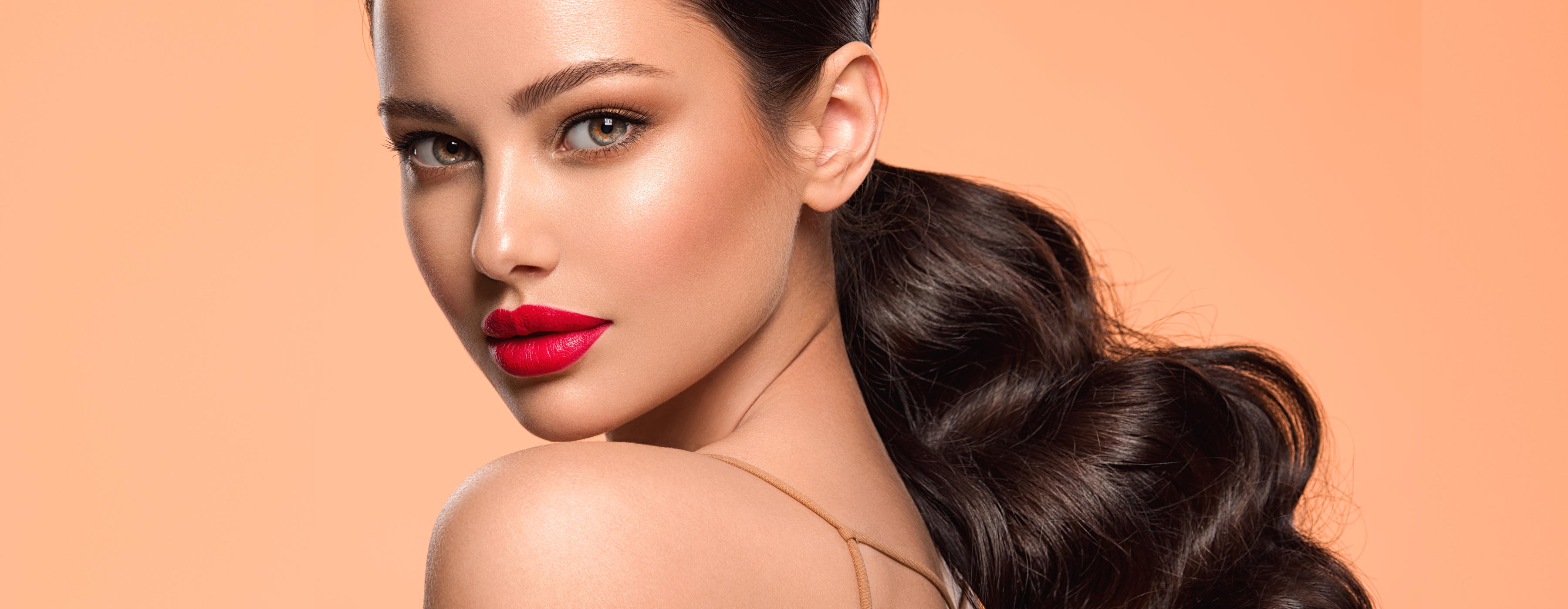Make e Hair para Festas e Eventos - Foto de modelo maquiada e cabelos presos, olhando sobre ombro esquerdo e lábios com batom vermelho.