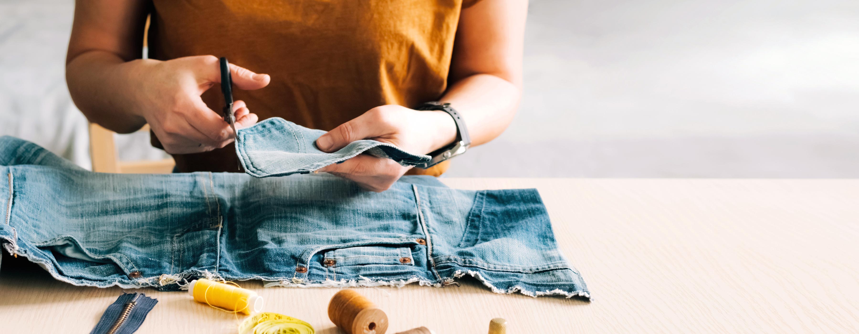 Upcycling: transformação de peças. Foto em close de mãos de uma mulher cortando bolso de calça jeans.