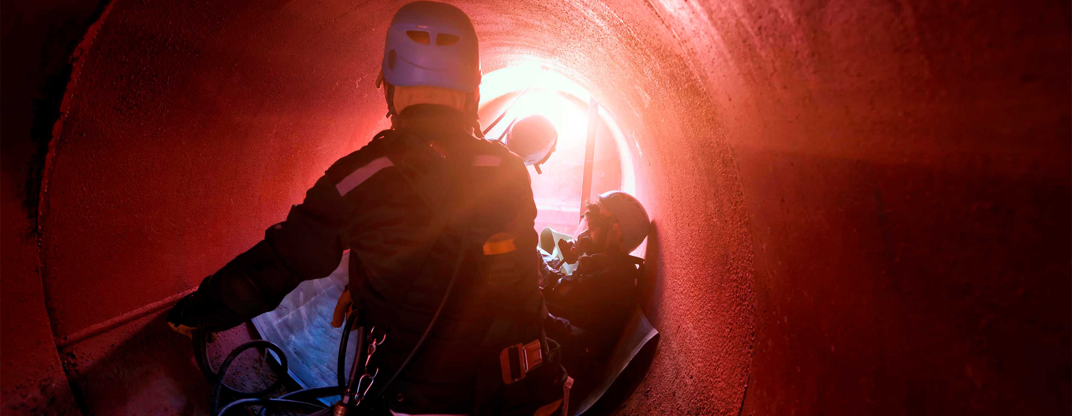 Foto de pessoas trabalhando com equipamentos de proteção em local com pouco espaço e pouca ventilação.
