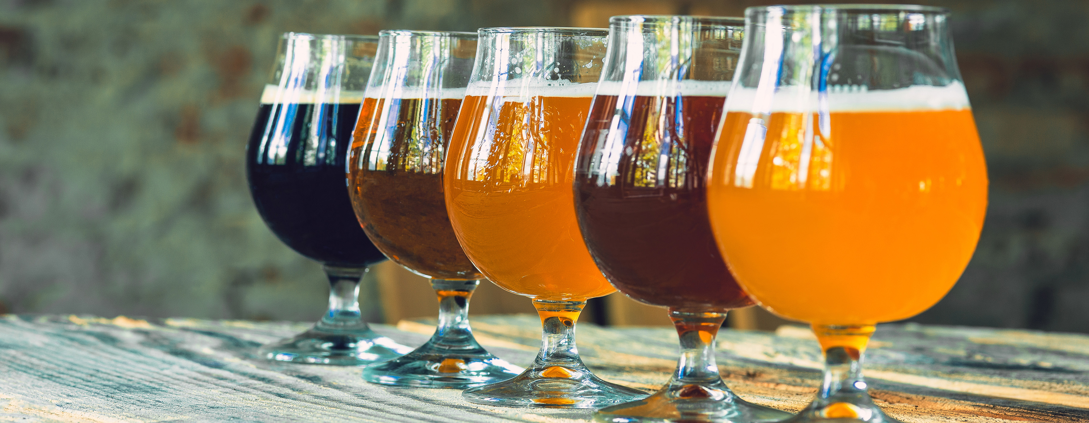 Formação de Sommelier: escolas e estilos cervejeiros. Foto de cinco copos de cervejas de tipos e cores diferentes, sobre uma base de madeira.