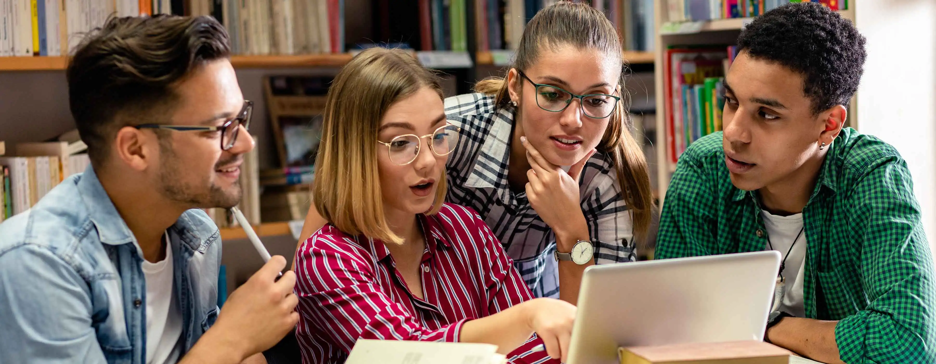 Espanhol Avançado - níveis 1 e 2. Foto de quatro jovens ao redor de uma mesa com livros e notebook em uma biblioteca.