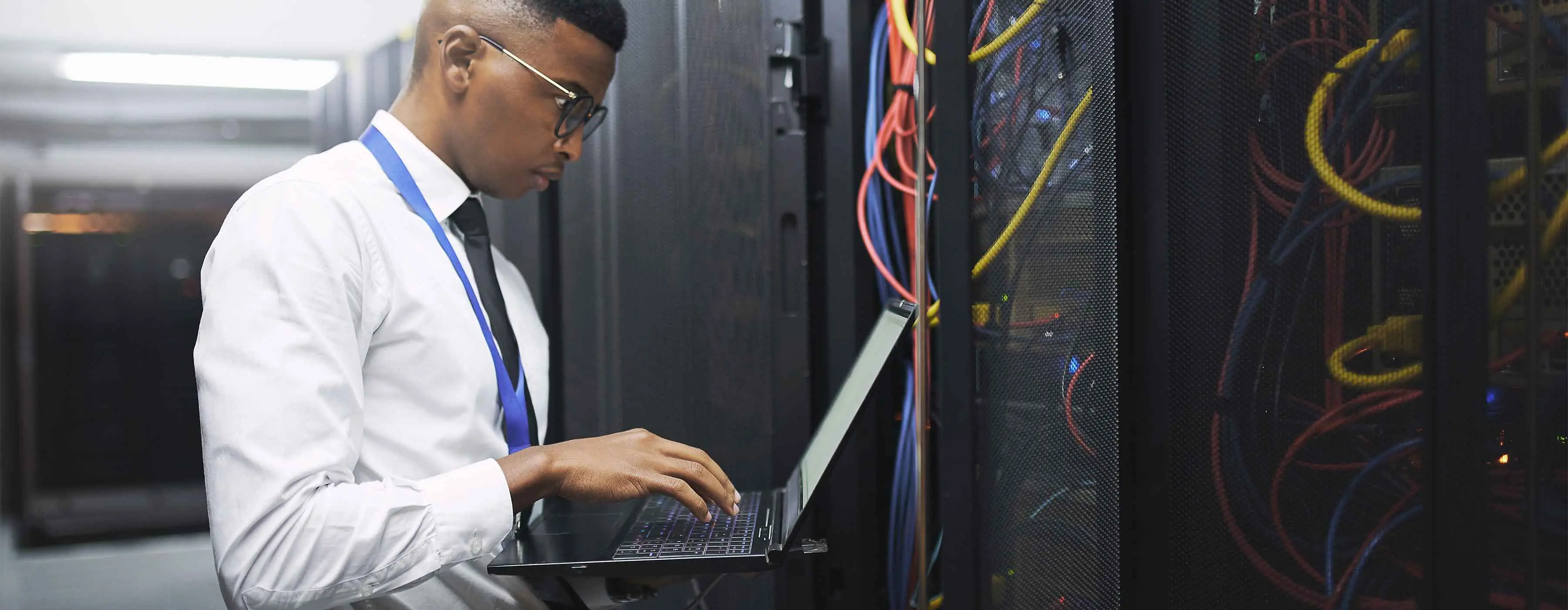 Foto de homem segurando notebook em frente a equipamento de cabeamento