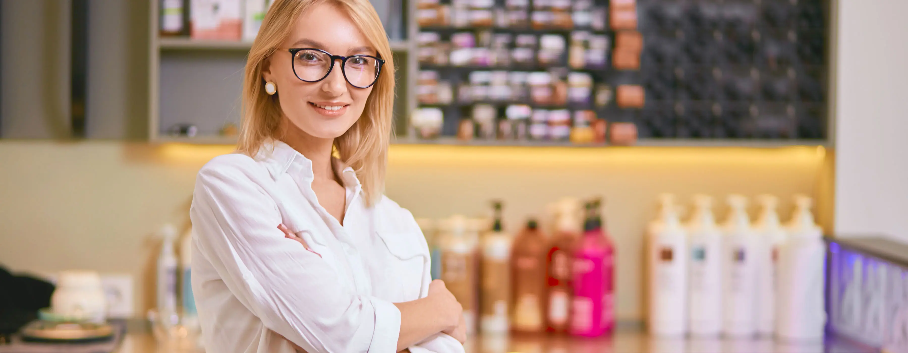 Foto de mulher sorrindo em frente a produtos de beleza.