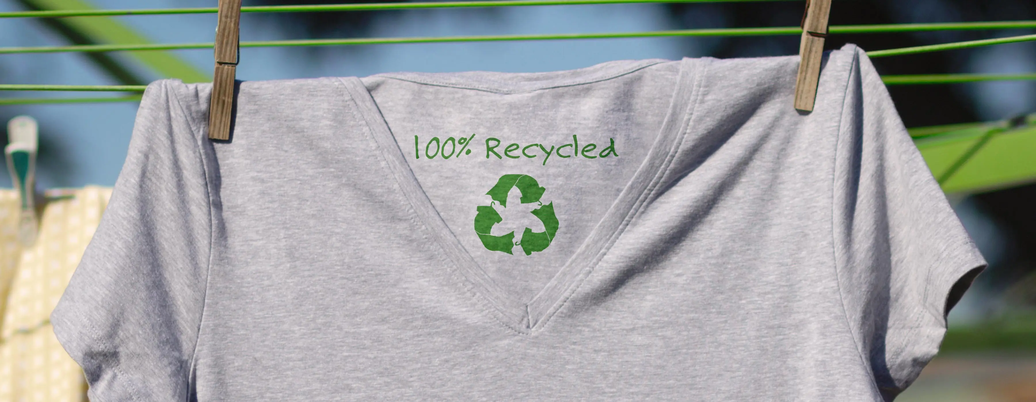 Foto de camiseta pendurada em varal escrito dentro dela 100% recycled e símbolo de reciclagem.