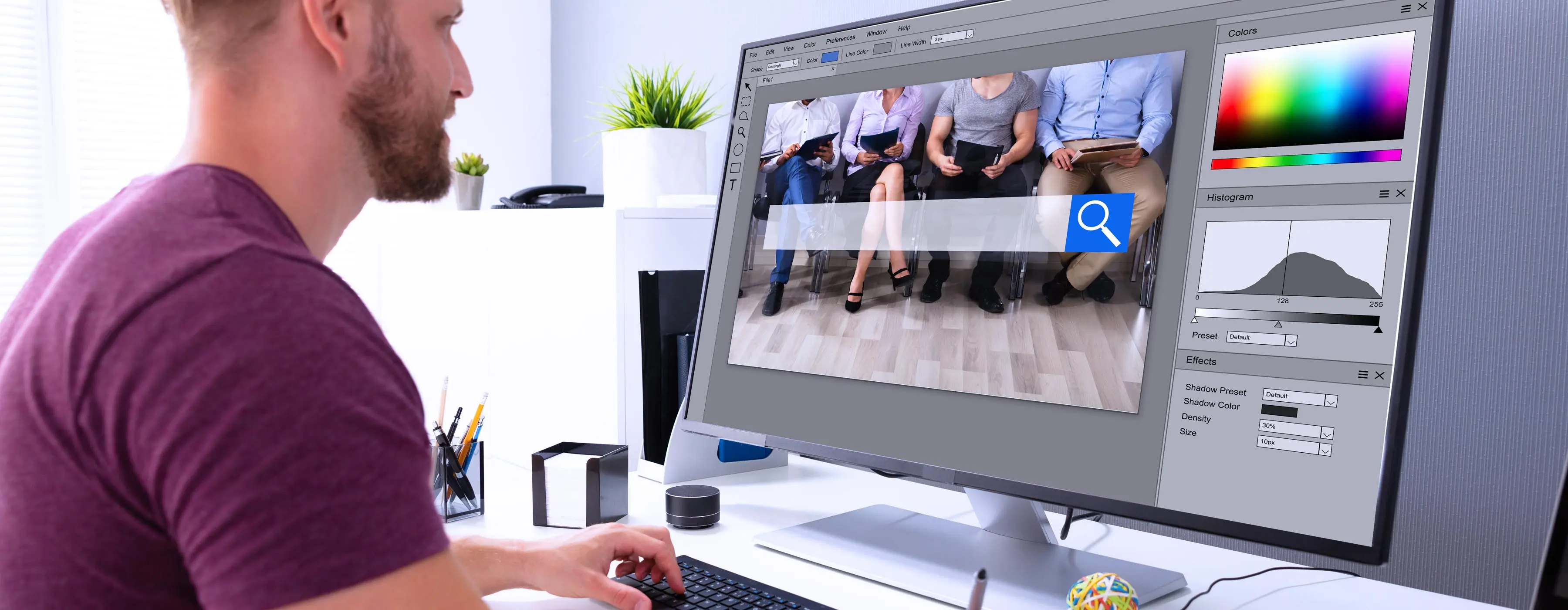 Foto de um homem sentado em frente para um monitor de computador editando imagem.