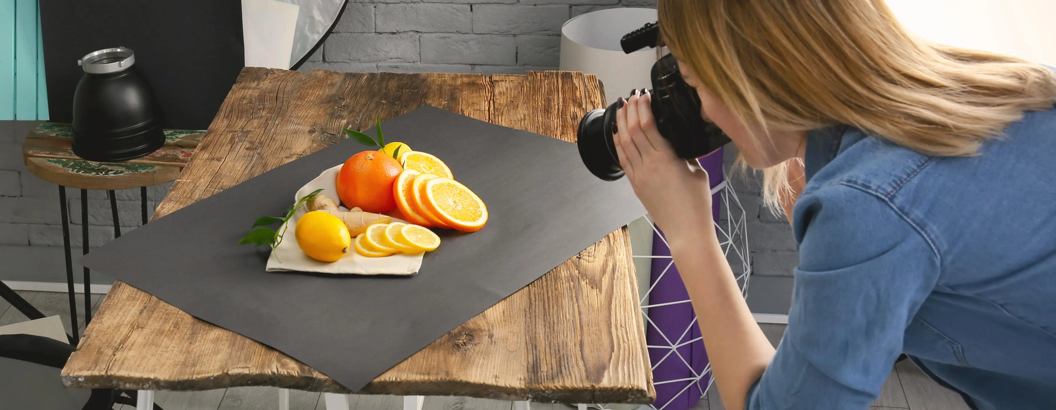 Foto de mulher de costas, fotografando frutas cortadas sobre uma mesa.