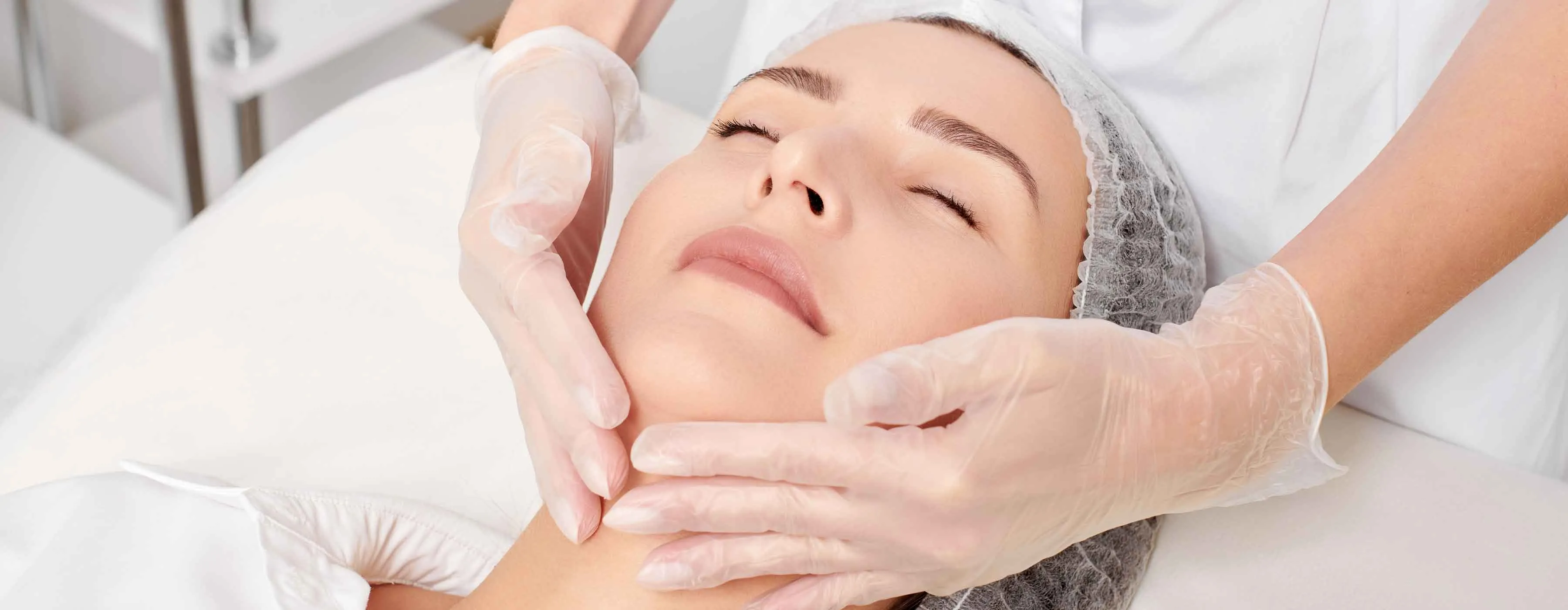 Mulher deitada em maca recebe massagem facial.